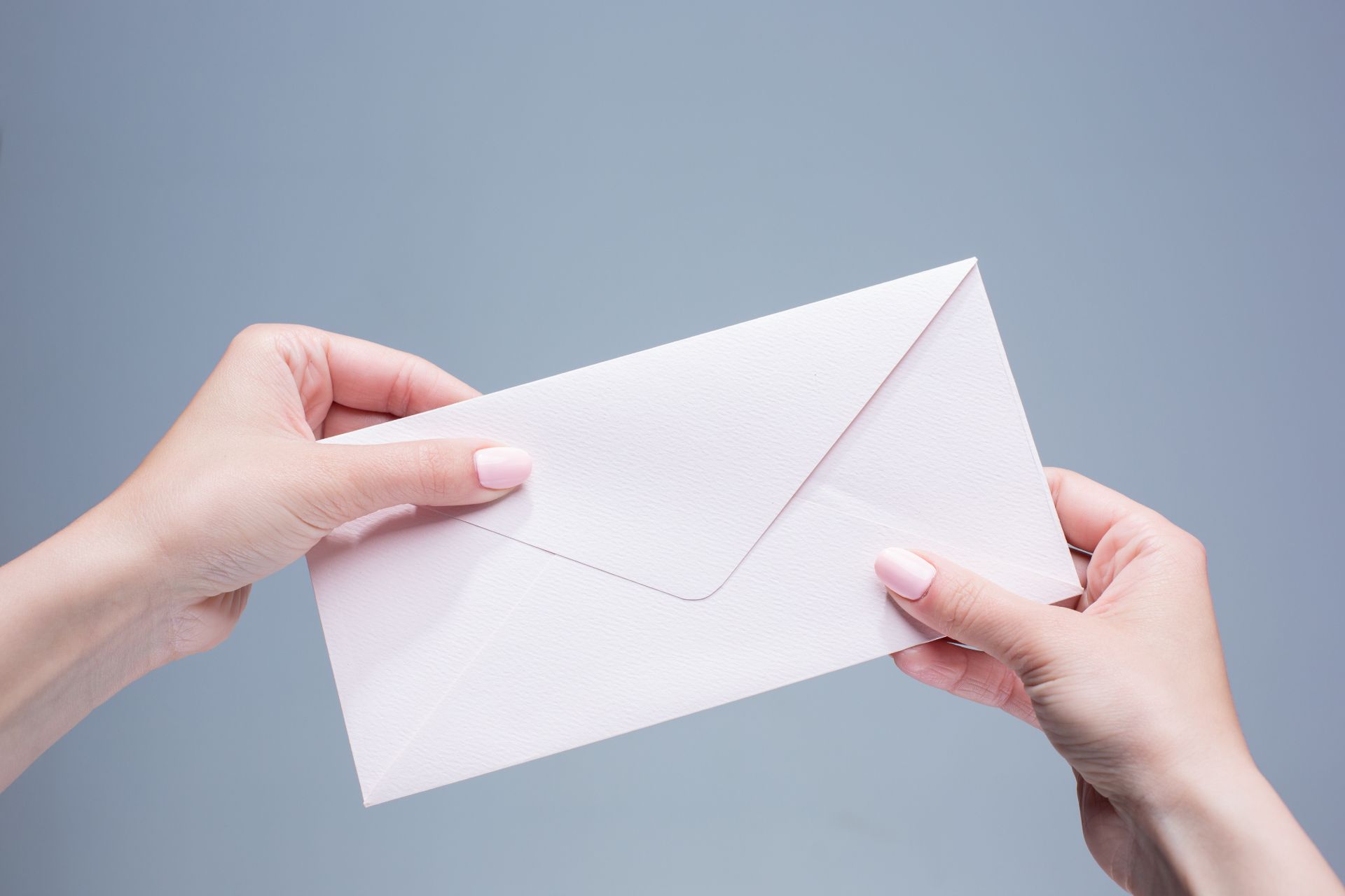female-hands-with-envelope-against-gray-background